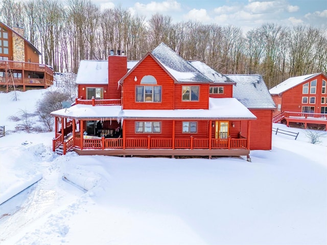 snow covered back of property featuring covered porch and a chimney