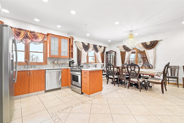 kitchen with brown cabinets, light countertops, appliances with stainless steel finishes, glass insert cabinets, and a peninsula