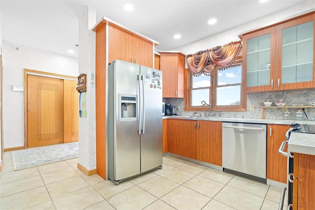 kitchen featuring glass insert cabinets, appliances with stainless steel finishes, backsplash, light countertops, and a sink