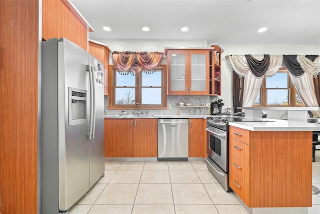 kitchen with light tile patterned floors, glass insert cabinets, appliances with stainless steel finishes, light countertops, and a sink