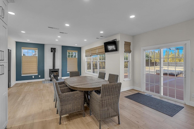 dining room with light wood-style flooring, plenty of natural light, and a wood stove