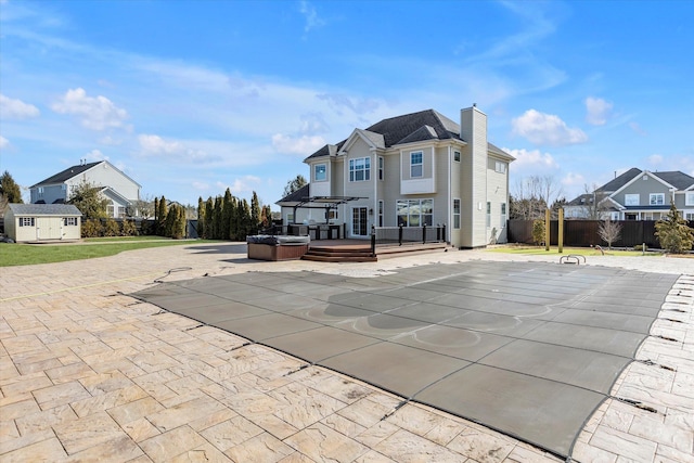 back of property featuring fence, a wooden deck, a hot tub, a patio, and a chimney