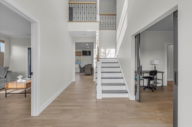 entrance foyer with ornamental molding, baseboards, light wood-style floors, and stairway