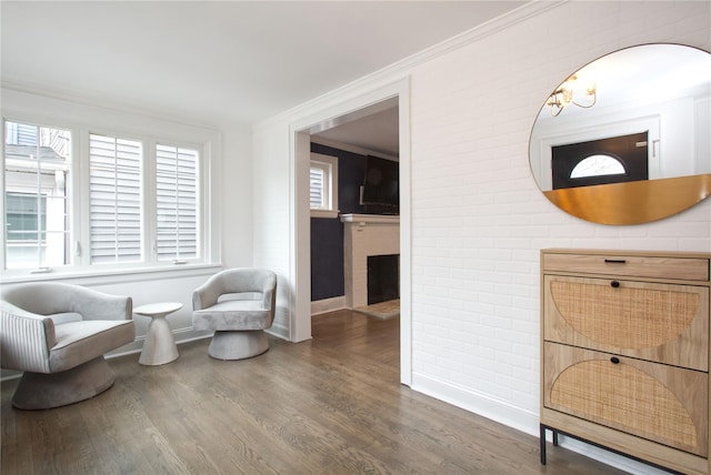 sitting room with ornamental molding, a fireplace, brick wall, and wood finished floors