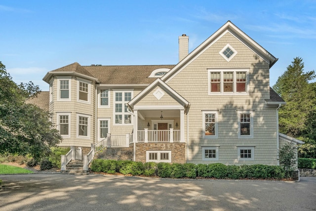 shingle-style home featuring stone siding, a chimney, and a shingled roof