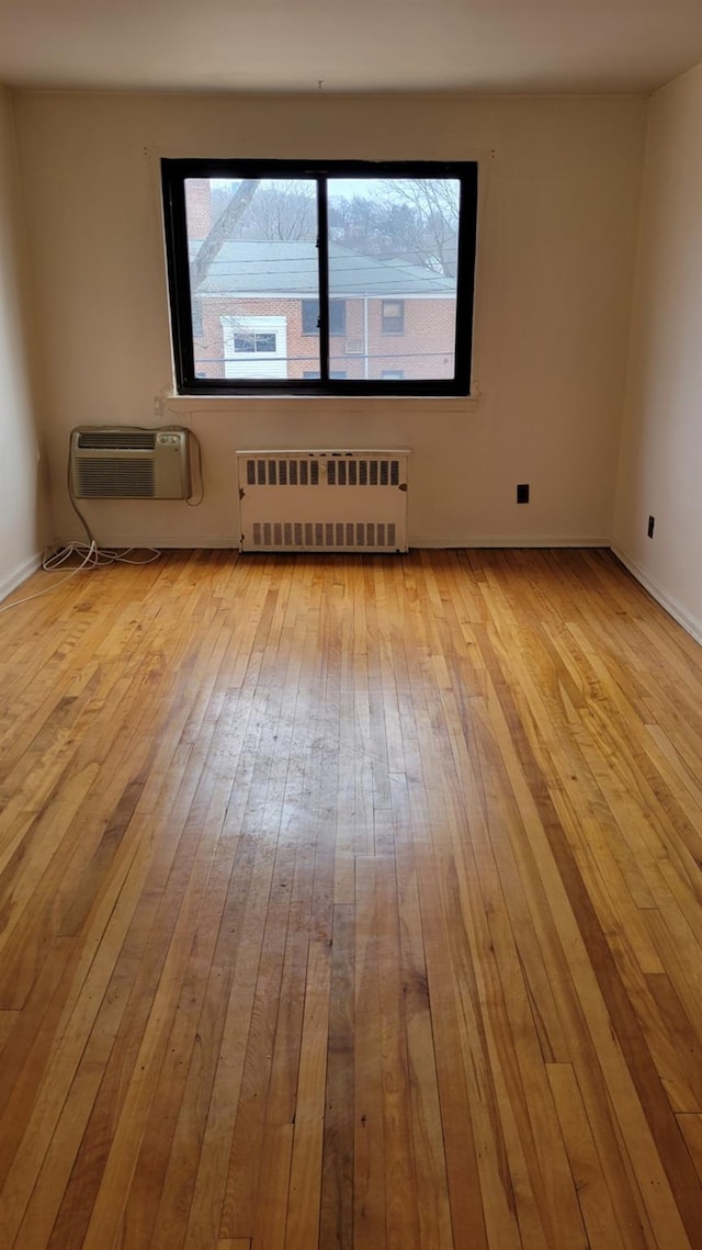 unfurnished room featuring a wealth of natural light, wood-type flooring, a wall unit AC, and radiator heating unit