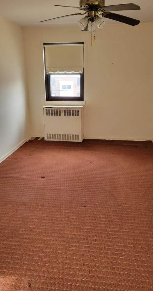 carpeted empty room featuring a ceiling fan and radiator heating unit