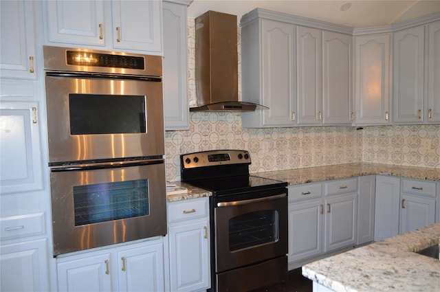 kitchen with wall chimney range hood, appliances with stainless steel finishes, white cabinets, and decorative backsplash