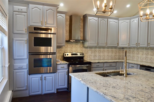 kitchen featuring wall chimney range hood, pendant lighting, stainless steel appliances, and light stone counters