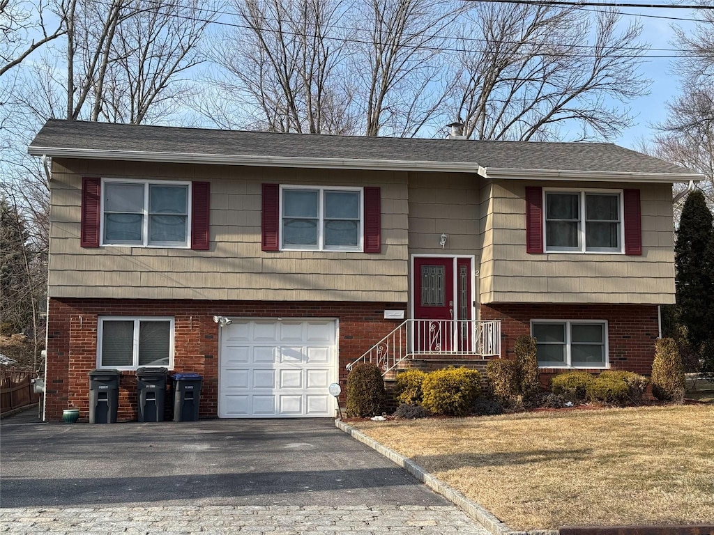 split foyer home featuring aphalt driveway, a garage, brick siding, and a front yard