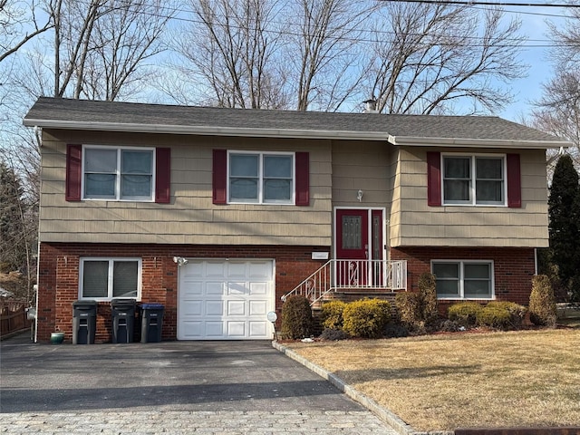 split foyer home featuring aphalt driveway, a garage, brick siding, and a front yard