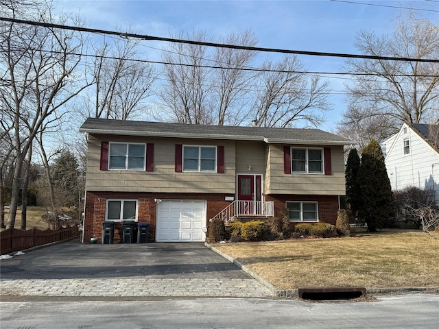 split foyer home featuring a front yard, fence, driveway, an attached garage, and brick siding