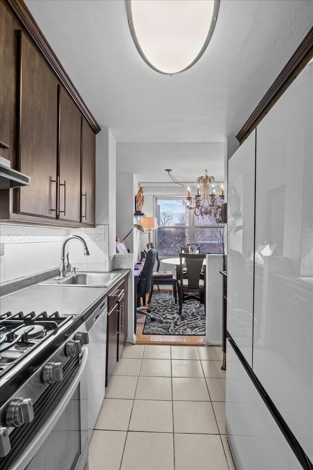 kitchen with appliances with stainless steel finishes, dark brown cabinets, a notable chandelier, light tile patterned floors, and sink