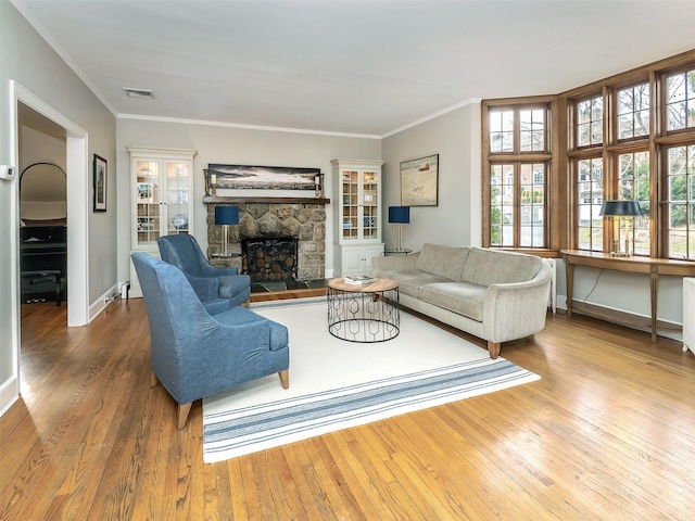 living room with hardwood / wood-style flooring, visible vents, ornamental molding, and a stone fireplace