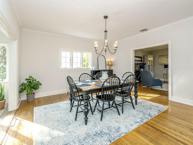 dining area with a notable chandelier, wood finished floors, visible vents, and crown molding