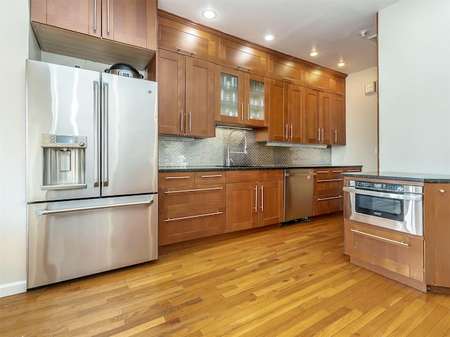 kitchen featuring light wood finished floors, decorative backsplash, appliances with stainless steel finishes, brown cabinetry, and a sink