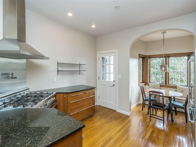 kitchen with brown cabinets, wall chimney exhaust hood, light wood-style floors, gas range, and baseboards