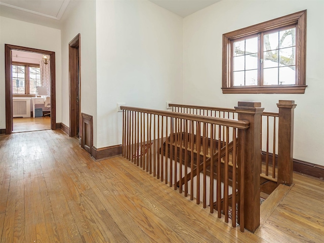 hallway featuring light wood-type flooring, radiator, baseboards, and an upstairs landing