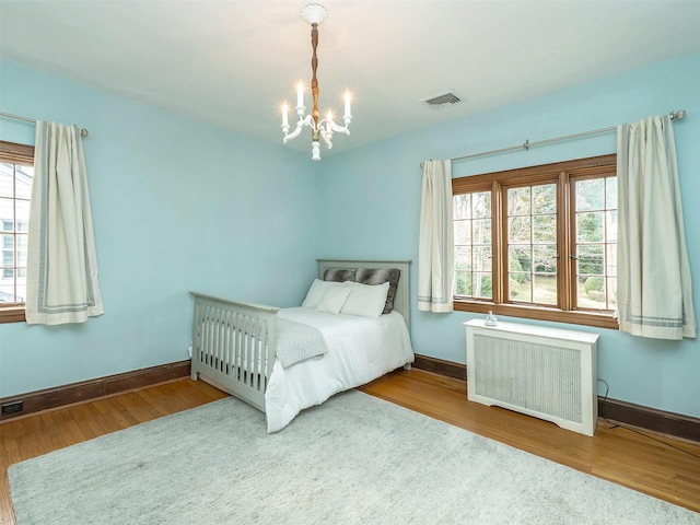 unfurnished bedroom featuring radiator heating unit, wood finished floors, visible vents, and an inviting chandelier