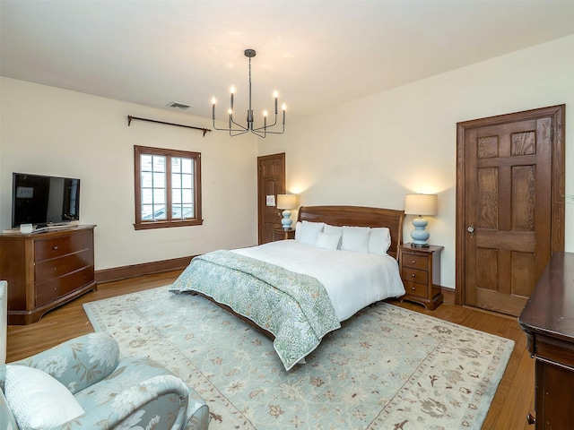 bedroom featuring baseboards, a notable chandelier, visible vents, and wood finished floors