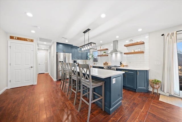 kitchen with light countertops, blue cabinetry, wall chimney range hood, open shelves, and stainless steel fridge