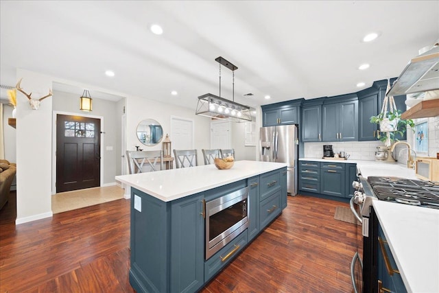 kitchen with appliances with stainless steel finishes, light countertops, blue cabinets, and dark wood-style floors