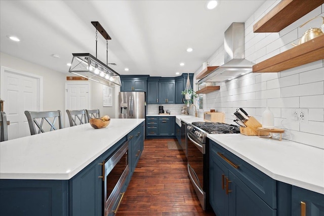 kitchen featuring blue cabinets, wall chimney exhaust hood, appliances with stainless steel finishes, and light countertops