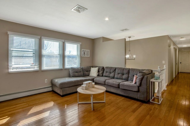 living room featuring attic access, visible vents, wood-type flooring, a baseboard heating unit, and a notable chandelier