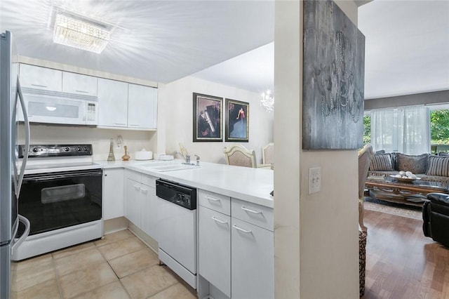 kitchen featuring kitchen peninsula, sink, white appliances, light tile patterned floors, and white cabinets