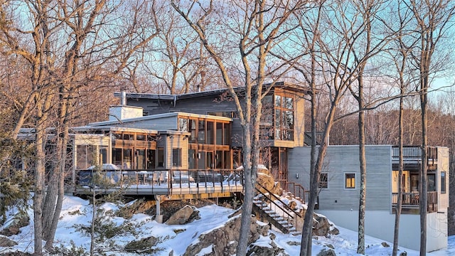 snow covered house featuring stairs, a chimney, and a wooden deck