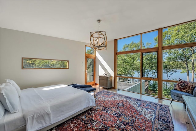 bedroom featuring expansive windows, a water view, an inviting chandelier, and wood finished floors