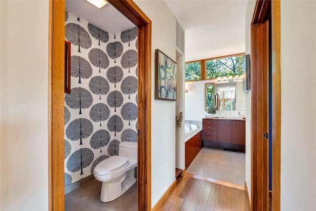 bathroom with a garden tub, toilet, wood finished floors, visible vents, and vanity