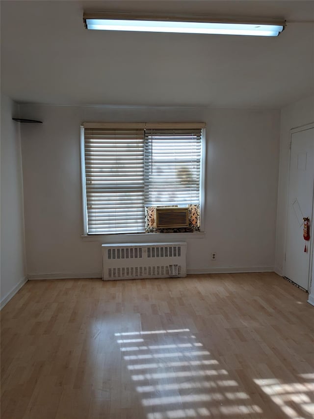 unfurnished room featuring baseboards, cooling unit, wood finished floors, and radiator