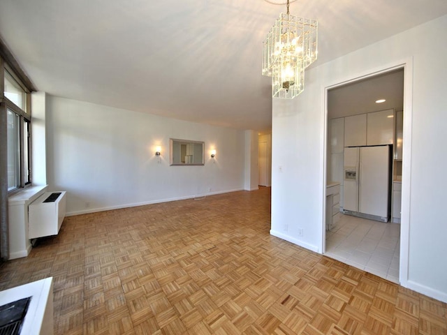 spare room featuring a chandelier, radiator heating unit, and baseboards