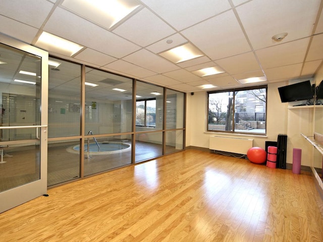 interior space with a healthy amount of sunlight, light wood finished floors, radiator heating unit, and a drop ceiling