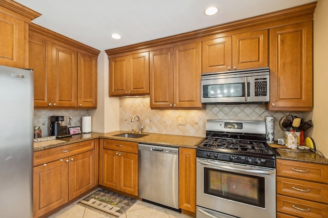 kitchen with dark stone countertops, appliances with stainless steel finishes, brown cabinets, and a sink