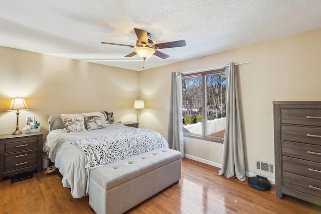 bedroom with baseboards, visible vents, ceiling fan, wood finished floors, and a textured ceiling