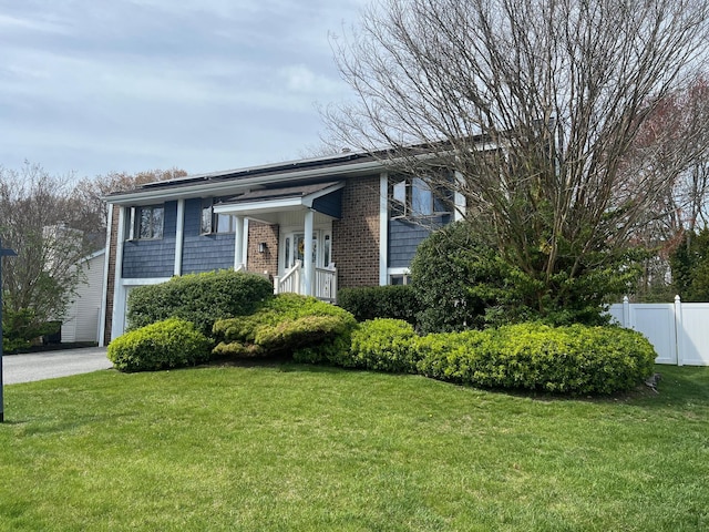 bi-level home featuring fence, brick siding, and a front lawn
