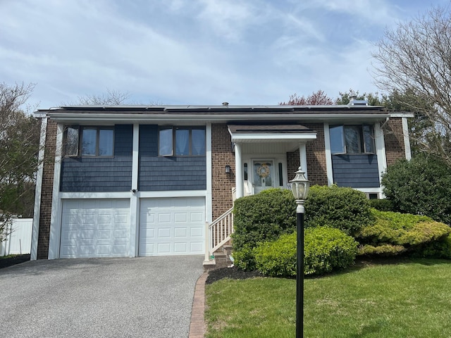 split foyer home with brick siding, solar panels, an attached garage, and aphalt driveway