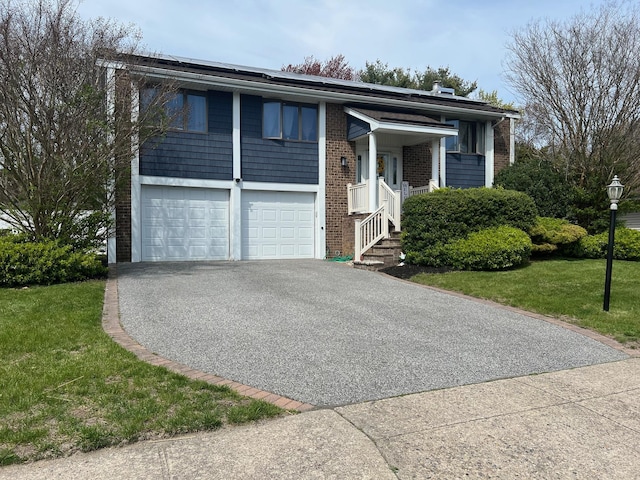 raised ranch featuring a front lawn, a garage, aphalt driveway, brick siding, and solar panels