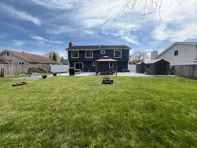 back of house featuring a patio, a fenced backyard, a storage shed, a gazebo, and a fire pit