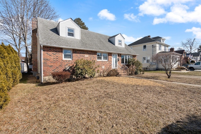 view of front of house with roof with shingles, a front lawn, and brick siding