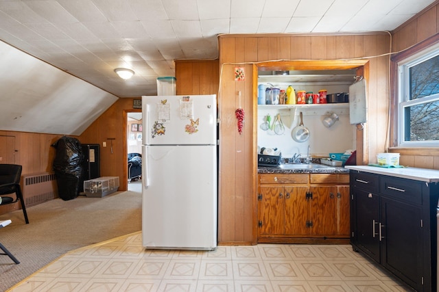 kitchen with radiator heating unit, freestanding refrigerator, a sink, wood walls, and dark cabinetry