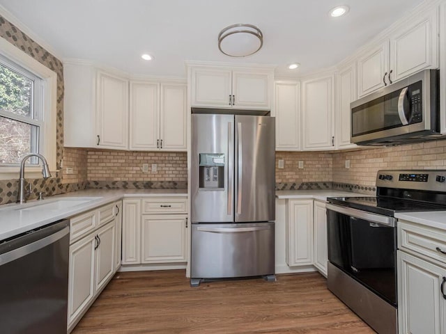 kitchen with stainless steel appliances, tasteful backsplash, light countertops, a sink, and wood finished floors