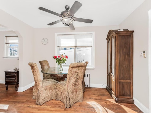 dining space featuring arched walkways, radiator heating unit, baseboards, and light wood finished floors