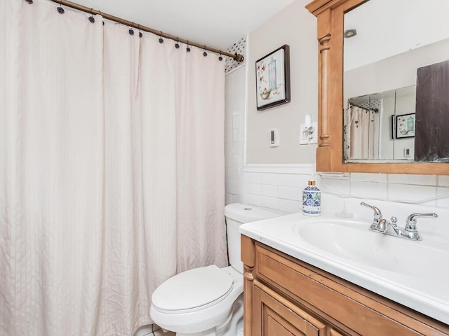 bathroom with toilet, a shower with shower curtain, vanity, tile walls, and wainscoting