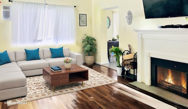 living area featuring a fireplace with flush hearth, an AC wall unit, and wood finished floors