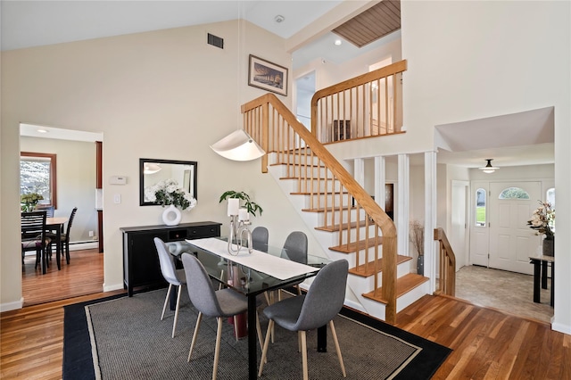 dining room with stairs, high vaulted ceiling, and wood finished floors