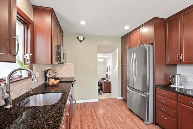 kitchen with a sink, stainless steel appliances, tasteful backsplash, dark stone countertops, and light wood finished floors