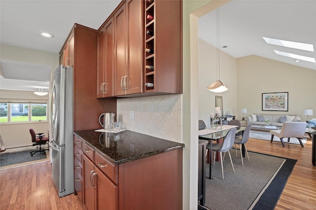 kitchen with freestanding refrigerator, light wood-type flooring, brown cabinets, and dark stone countertops